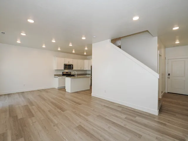 Spacious open-concept living area featuring wood-finish flooring, recessed lighting, and a white kitchen with an island