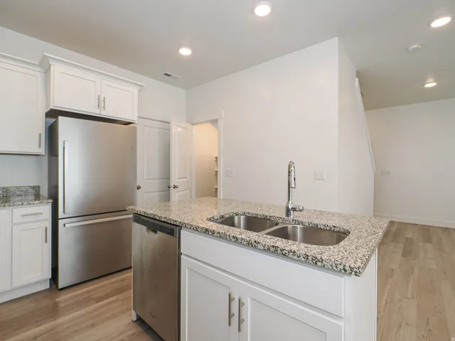 Kitchen island featuring a double basin stainless steel sink with a chrome faucet, granite-finish countertop, and white cabinetry