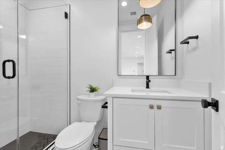 Bathroom featuring a glass-enclosed shower with white subway tile, a white vanity with a rectangular sink, a light-toned countertop, and matte black fixtures