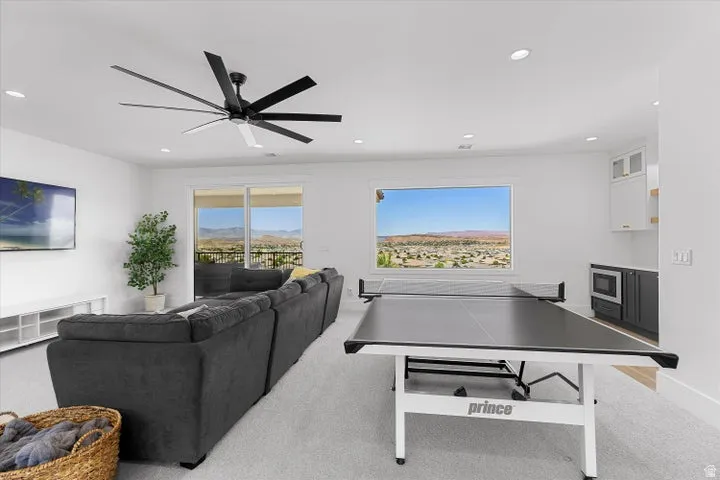 Spacious entertainment area featuring a large picture window, glass sliding doors, recessed lighting, and a built-in wet bar with a microwave