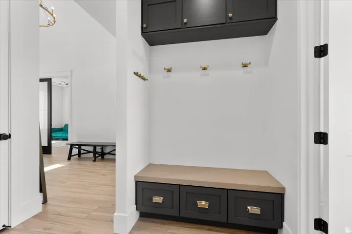 Custom mudroom featuring dark cabinetry with gold hardware, a built-in bench, and wall-mounted hooks