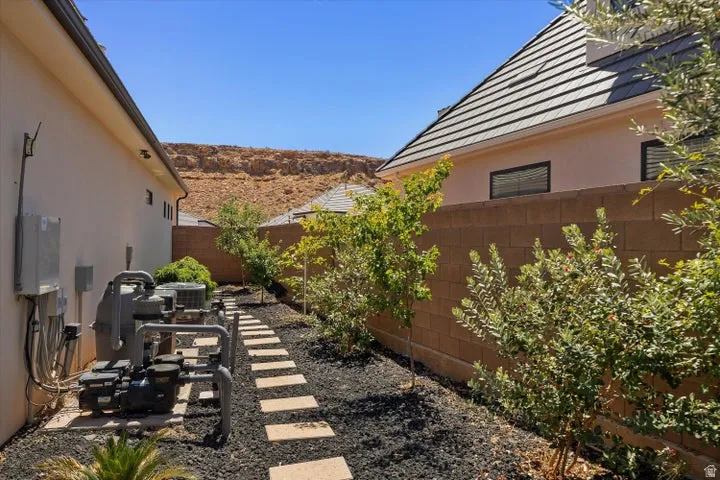 Outdoor utility area featuring integrated mechanical systems, a stone paver pathway, and landscaping with mature plantings