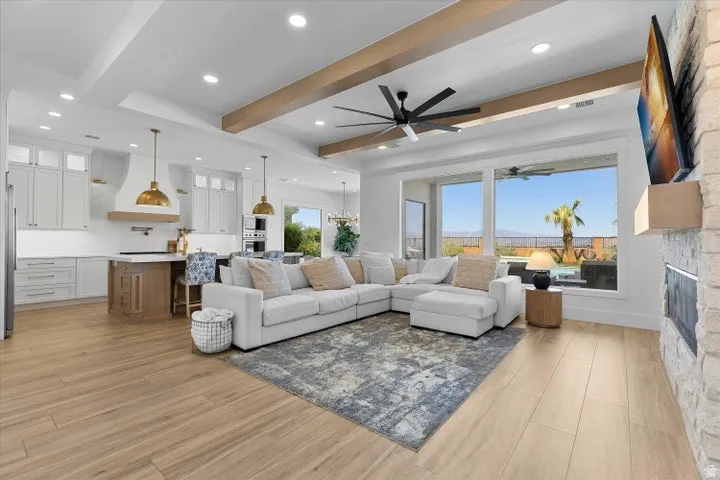 Open-concept living space featuring wood-finish flooring, a stone-clad fireplace, and expansive windows