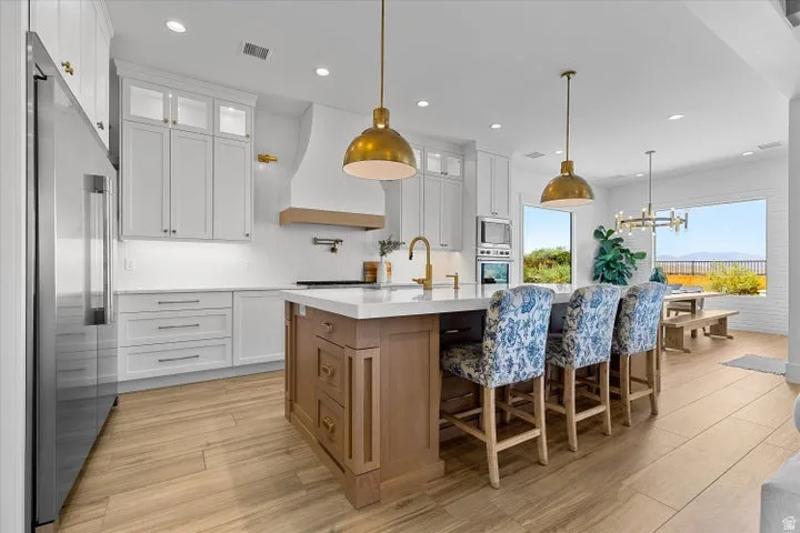 Modern kitchen featuring an expansive center island with seating, white shaker cabinetry, stainless steel appliances, and wood-finish flooring