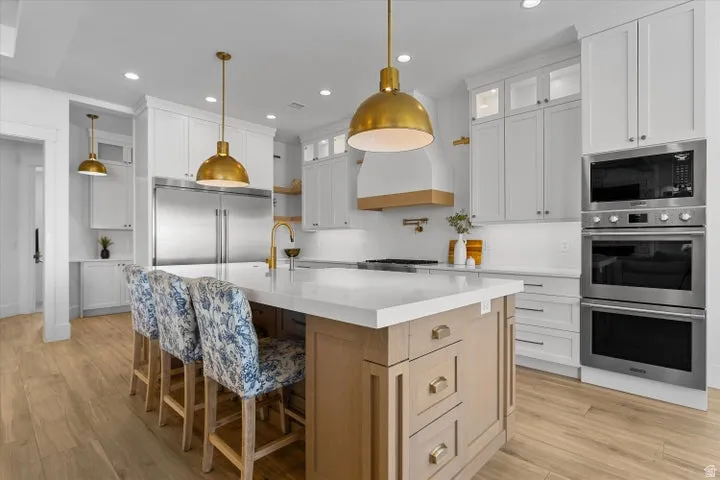 Gourmet kitchen featuring a substantial island with seating, integrated stainless steel appliances, a brass-toned faucet, and hardwood flooring