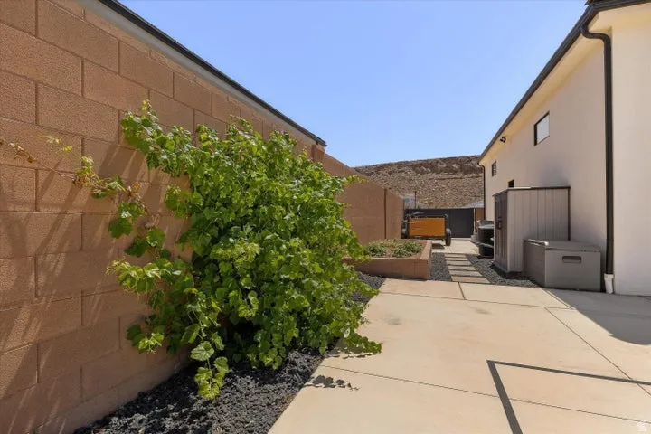 Exterior side yard featuring concrete paving, a raised planter bed, and a landscaped rock border