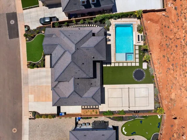 Expansive property featuring a multi-gabled dark gray roofline, a large outdoor swimming pool with integrated spa, a pickleball court, a putting green, and a concrete driveway