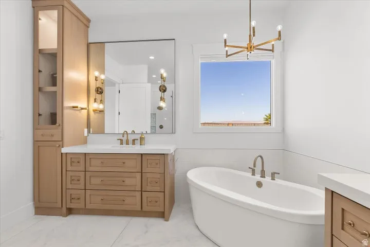 Bathroom featuring a freestanding soaking tub, single vanity with wood-finish cabinetry, built-in linen tower, large rectangular mirror, and an overhead chandelier light fixture