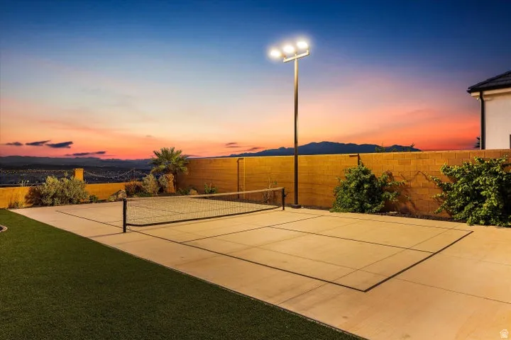 Private backyard featuring a concrete sport court with a net, artificial turf, and a towering light fixture
