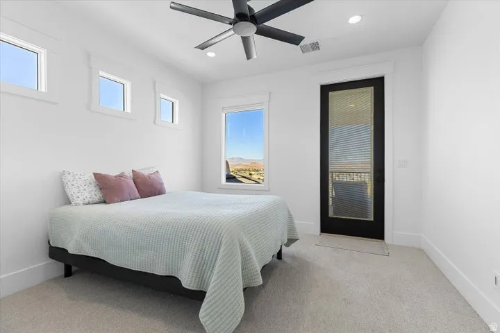 Contemporary room with light-colored carpeting, featuring a black ceiling fan with integrated lighting, recessed ceiling lights, and three transom windows