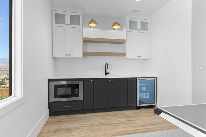 Wet bar featuring white upper cabinetry with glass inserts, dark base cabinetry, light countertops, and wood-finish flooring