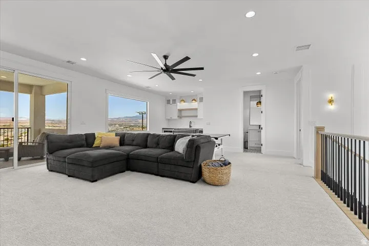 Open-concept loft area with light-toned carpeting, featuring a wet bar with white cabinetry and open shelving