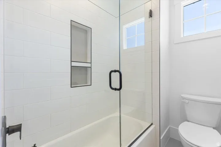 Bright bathroom featuring a glass-enclosed tub and shower combination with white subway tile surround, matte black fixtures, and built-in shower niche