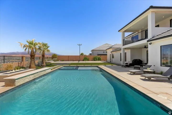 Expansive outdoor living area featuring a rectangular swimming pool with integrated spa, a fire feature, and a paved patio