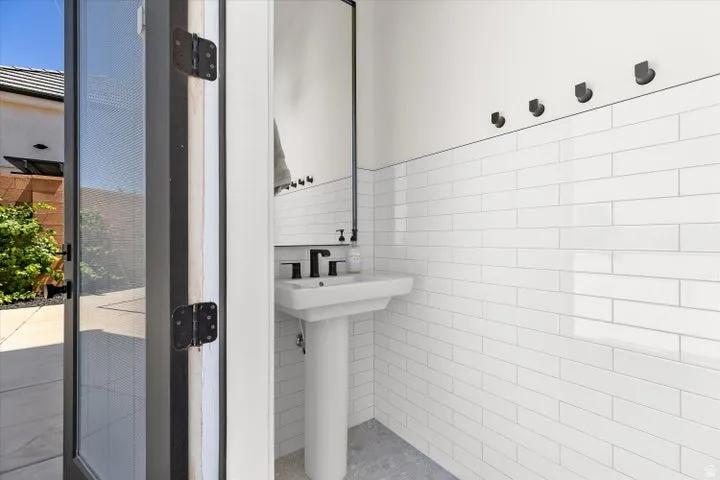 Pedestal sink with matte black faucet, wall-mounted mirror, white subway tile wainscoting, and four wall-mounted black hooks