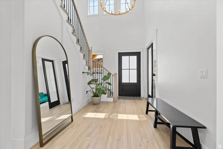 Two-story entryway with light wood-finish flooring, a dark-paneled front door with glass inserts, and a prominent staircase featuring dark iron railings
