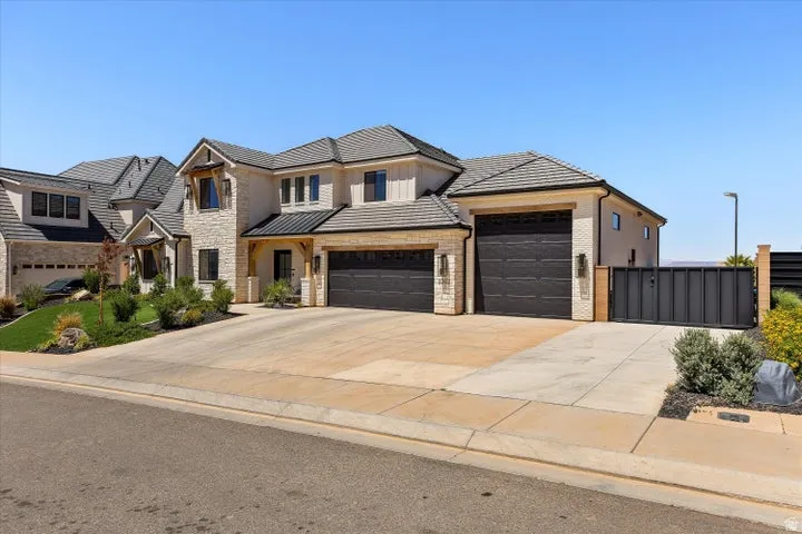 Contemporary architecture featuring a stone and stucco facade, dark tile roofing, multiple garage doors, a paved driveway, and a private side gate