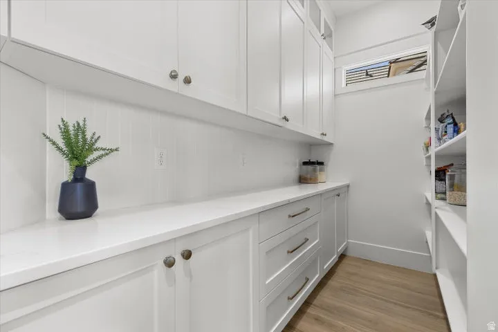 Expansive pantry featuring custom white cabinetry, integrated shelving, wood-finish flooring, a solid surface countertop, and a transom window