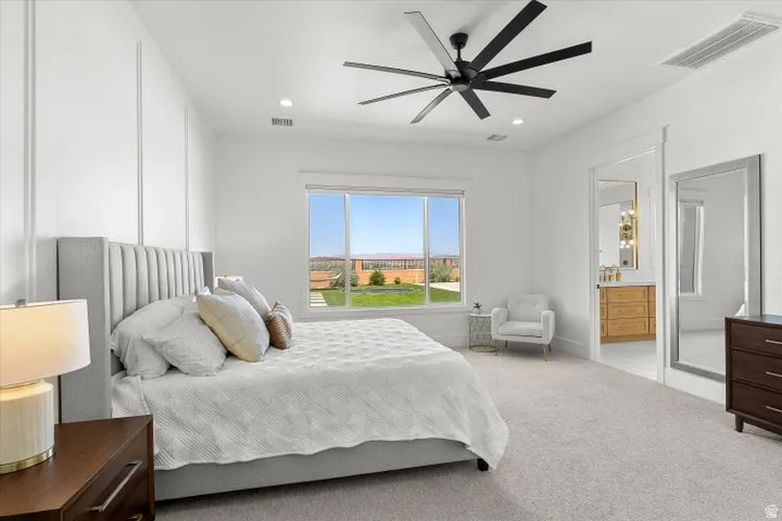 Spacious bedroom featuring plush carpet flooring, a large window offering outdoor scenery, and a modern ceiling fan