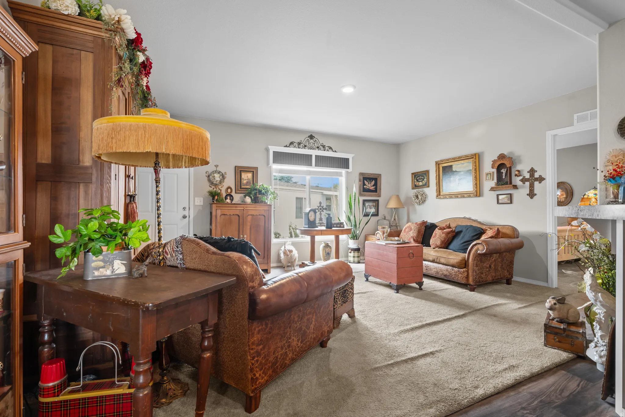 Spacious living area featuring light neutral wall tones, recessed lighting, a large window, and wood-finish flooring transitioning to carpet