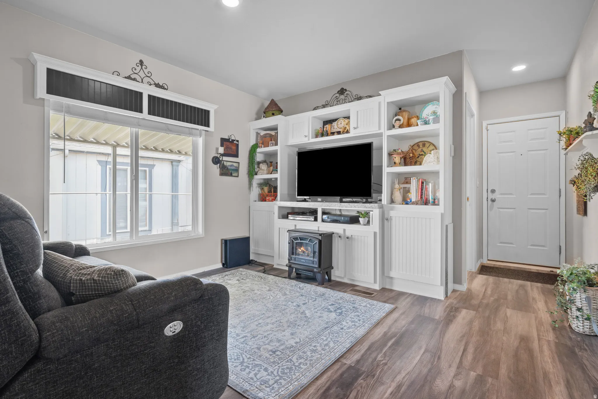 Living area featuring built-in white cabinetry with open shelving, wood-finish flooring, and a multi-pane window