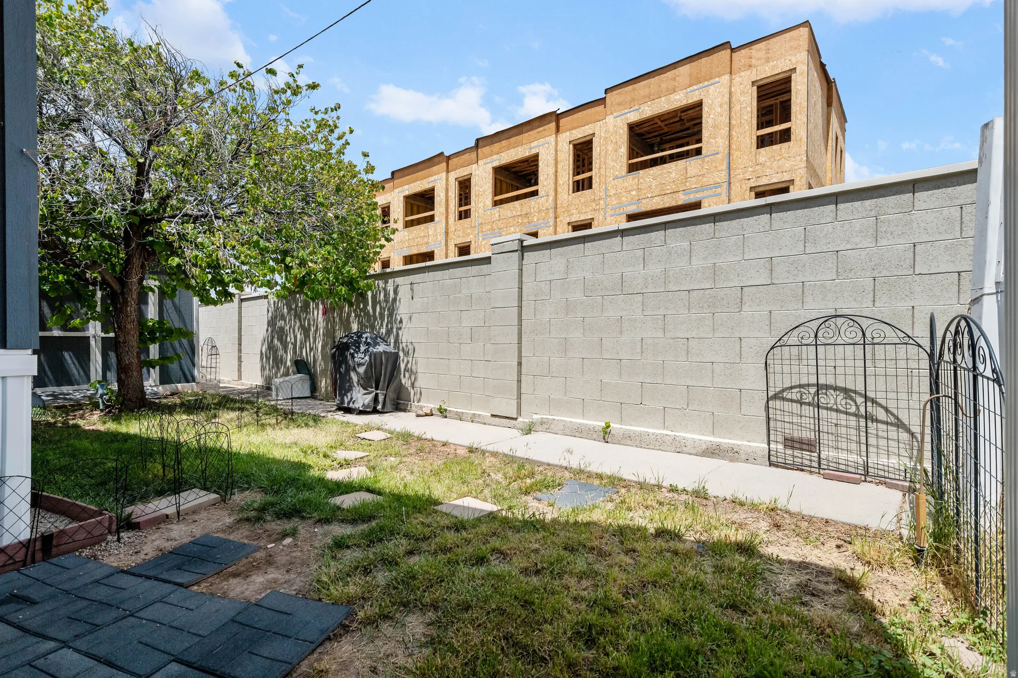 Private backyard space featuring a concrete block perimeter wall, a mature tree, a paved patio area, and stepping stones