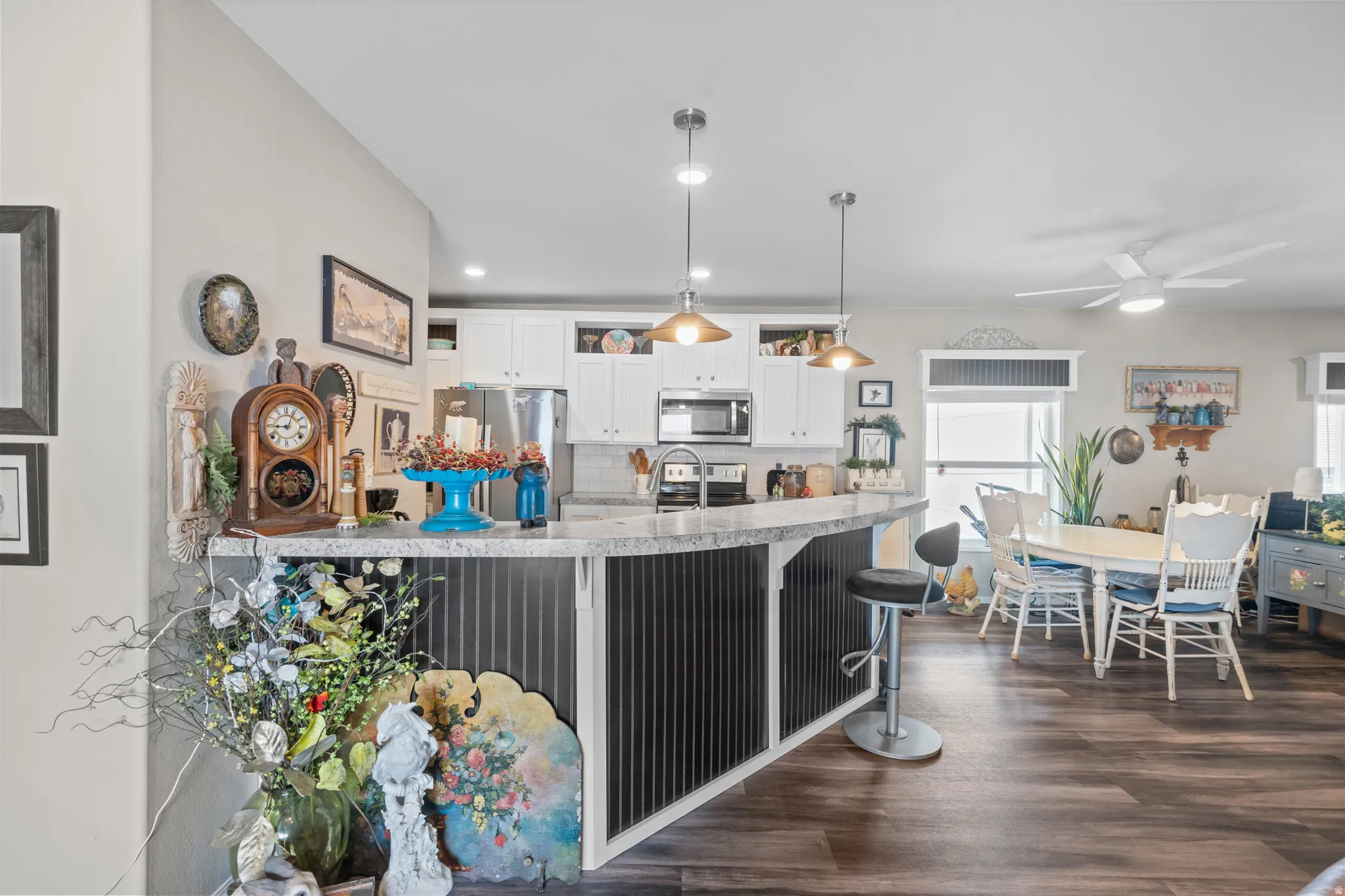 Open-concept kitchen and dining area featuring a breakfast bar with corrugated metal paneling, granite-look countertops, white cabinetry, and wood-finish flooring