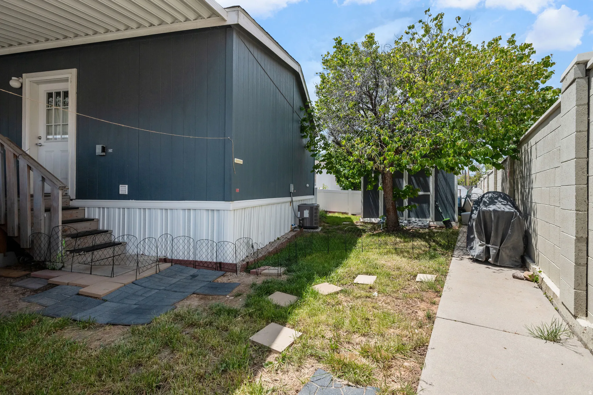 Side yard with an established tree, concrete pathway, and block wall fencing