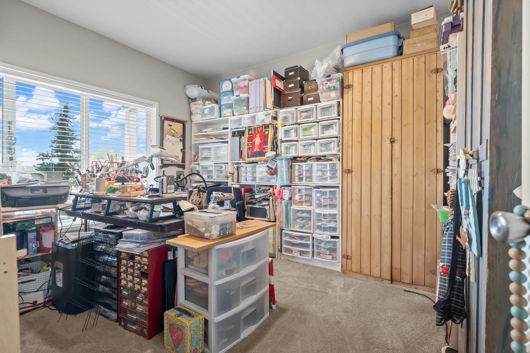 Room with a large window and horizontal blinds, featuring a built-in wood cabinet with vertical paneling