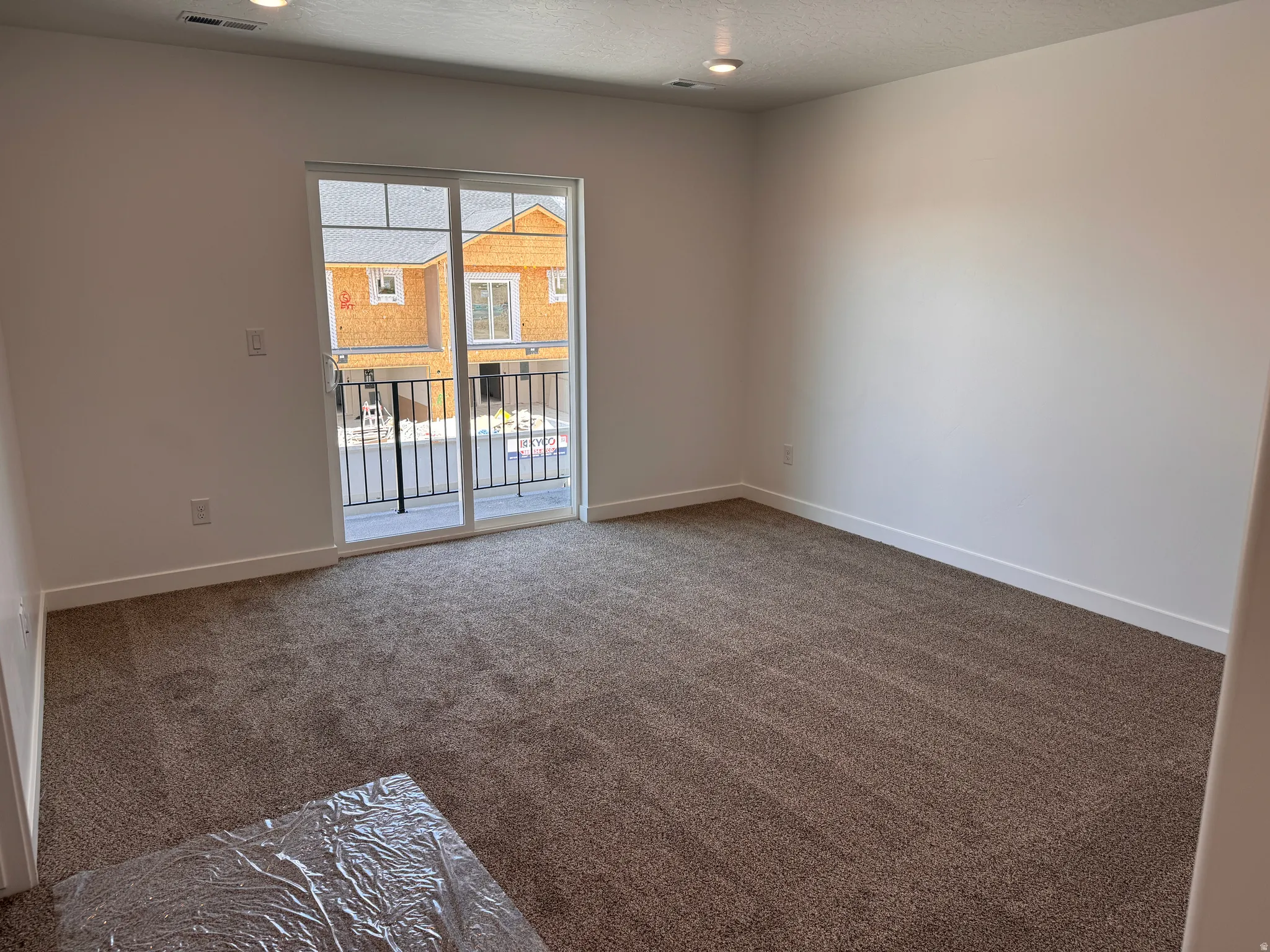 Carpeted room with a sliding glass door opening to an exterior balcony featuring a black metal railing