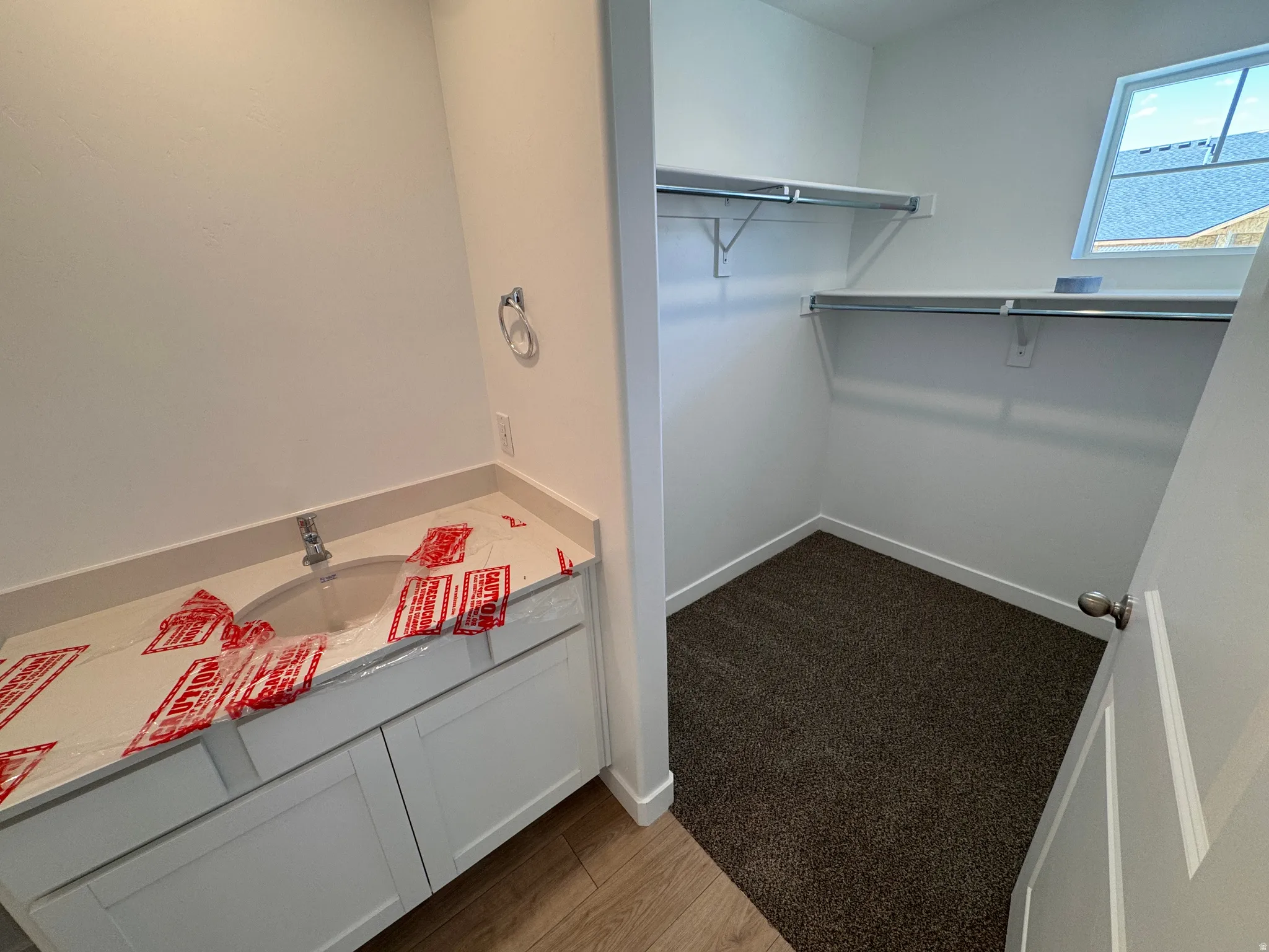 Bathroom vanity with a single sink and white cabinetry, accompanied by a separate closet space featuring a sloped ceiling and an upper window