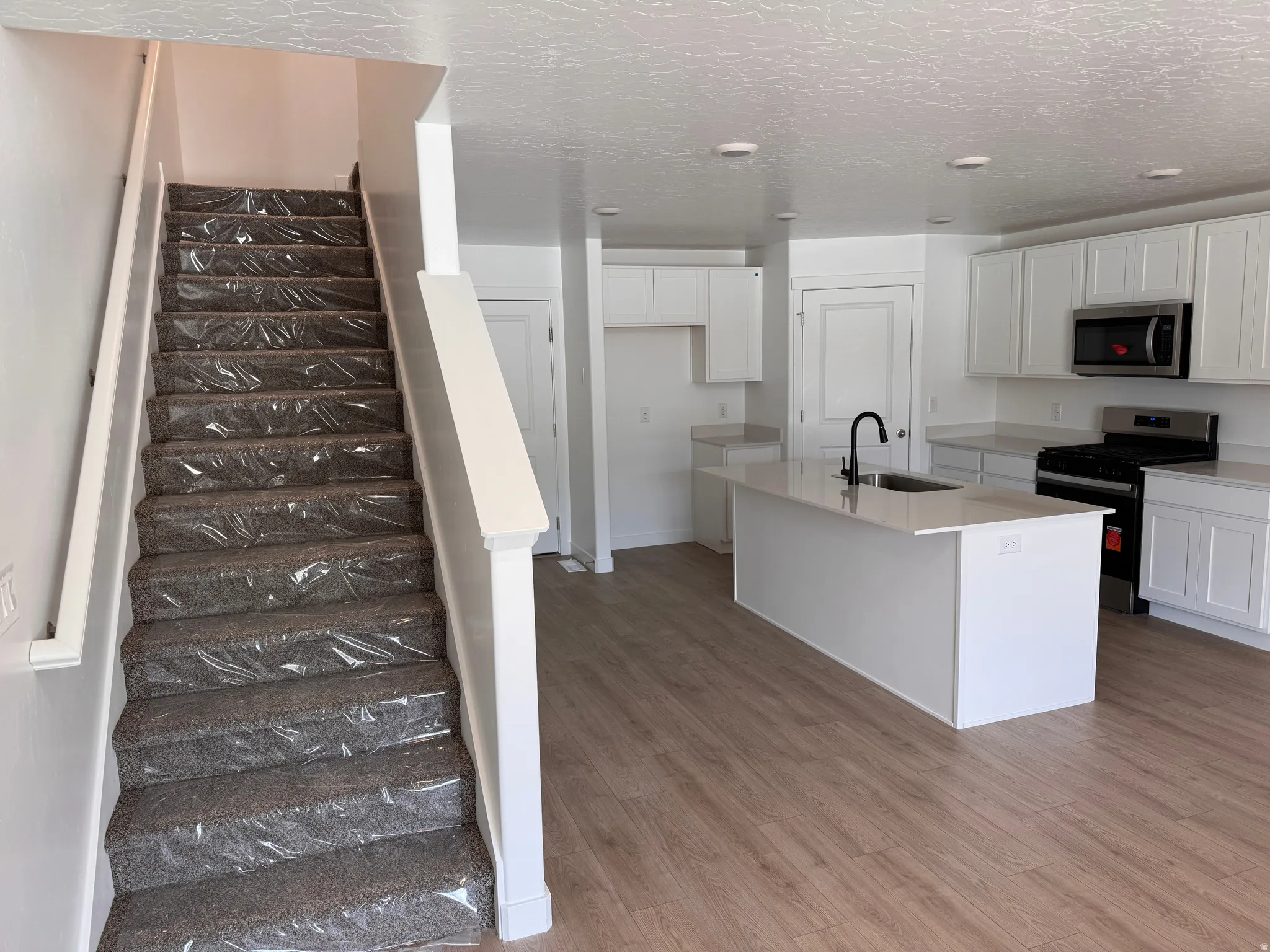 Open-concept living space with wood-finish flooring, a contemporary kitchen, and a carpeted staircase with white railings