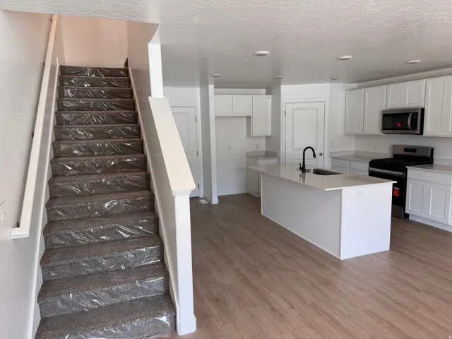 Open-concept living space with wood-finish flooring, a contemporary kitchen, and a carpeted staircase with white railings