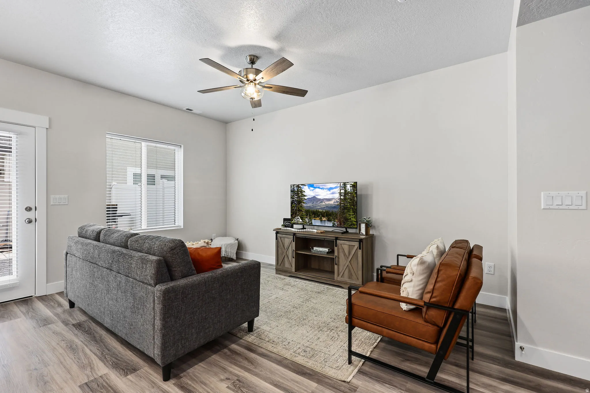 Spacious living area featuring wood-finish flooring, a contemporary ceiling fan, and a glass-paneled exterior door