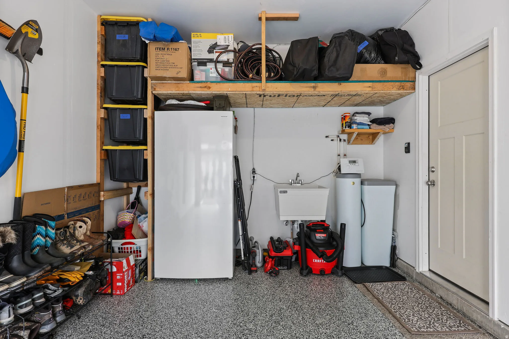 Garage featuring an epoxy-coated concrete floor, overhead storage shelving, a utility sink, and installed water filtration systems