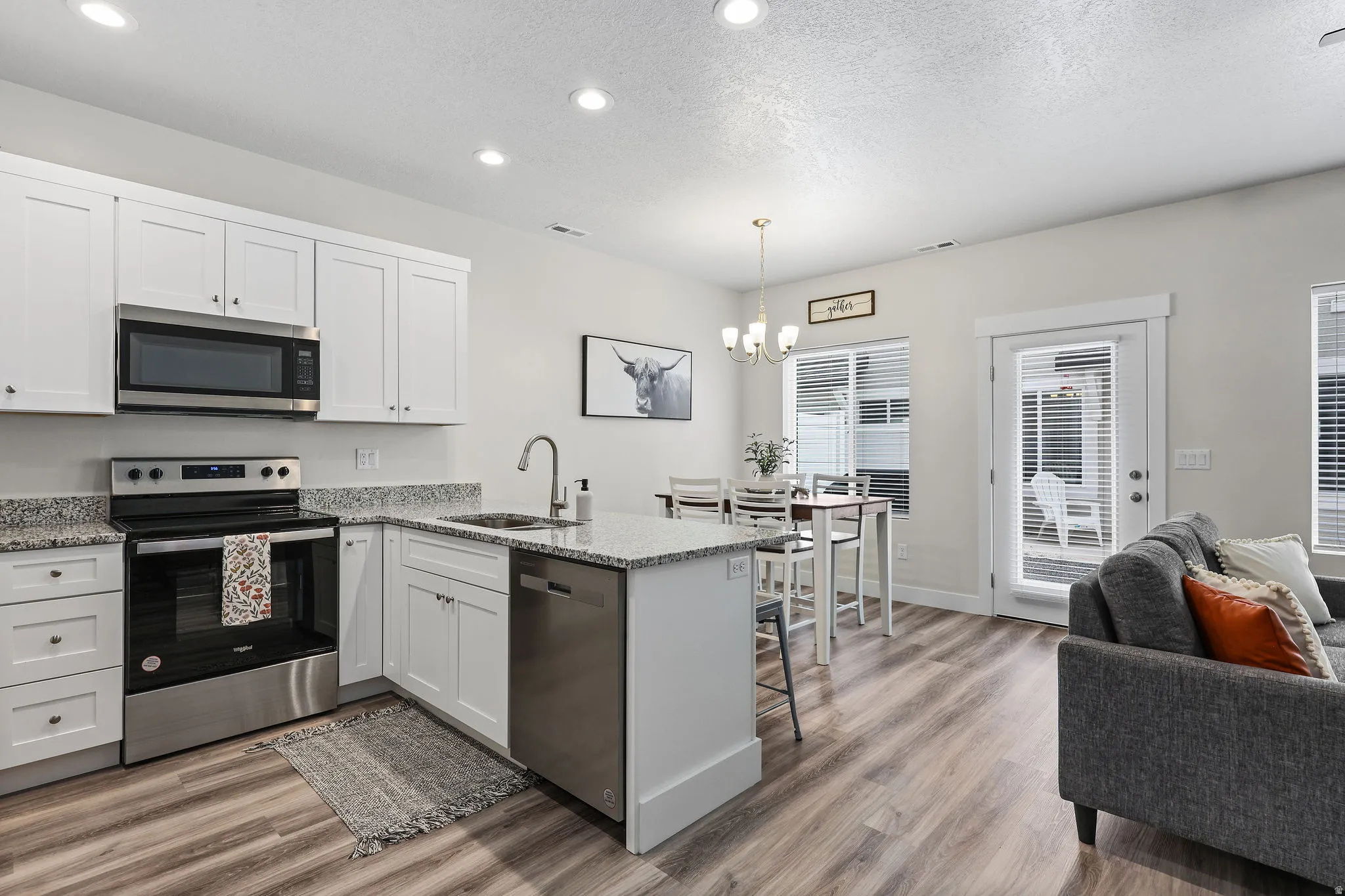 Modern kitchen featuring white cabinetry, granite countertops, and stainless steel appliances, including a microwave, range, and dishwasher
