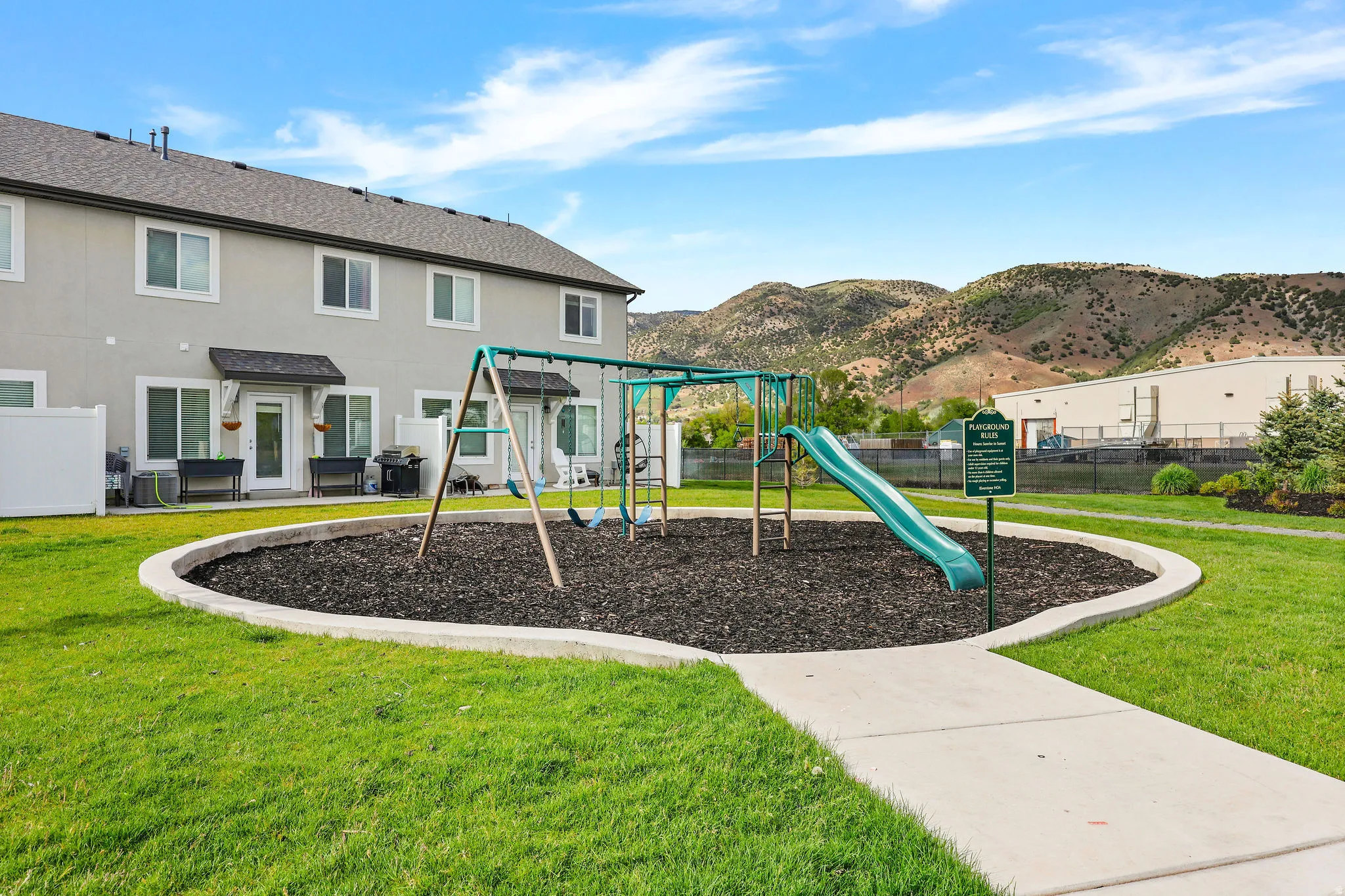 Community playground featuring a swing set and slide on a mulch ground cover, surrounded by manicured green space