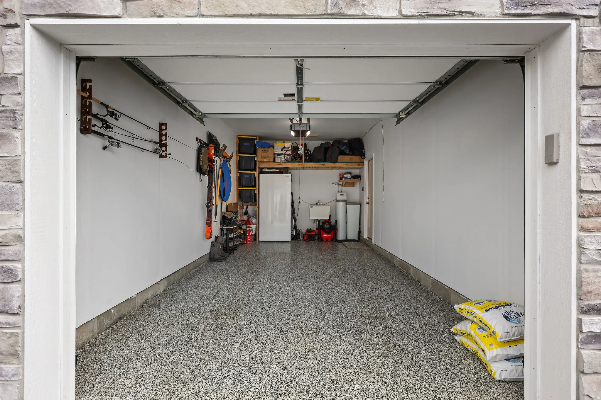 Spacious garage featuring stone-clad exterior entry, durable epoxy flooring, and ample overhead storage shelving