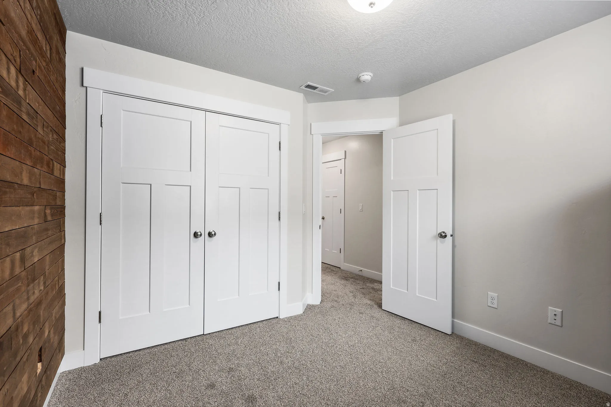 Bedroom featuring a wood accent wall, white paneled doors, neutral gray carpet, and light gray wall paint