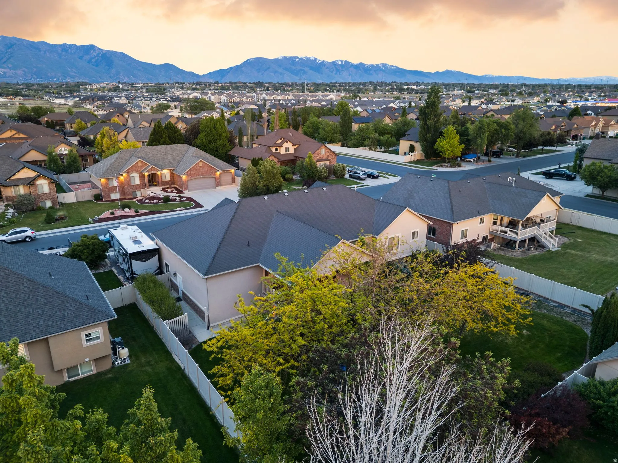 Spacious residential property featuring a large backyard with a covered deck, white vinyl fencing, and mature trees