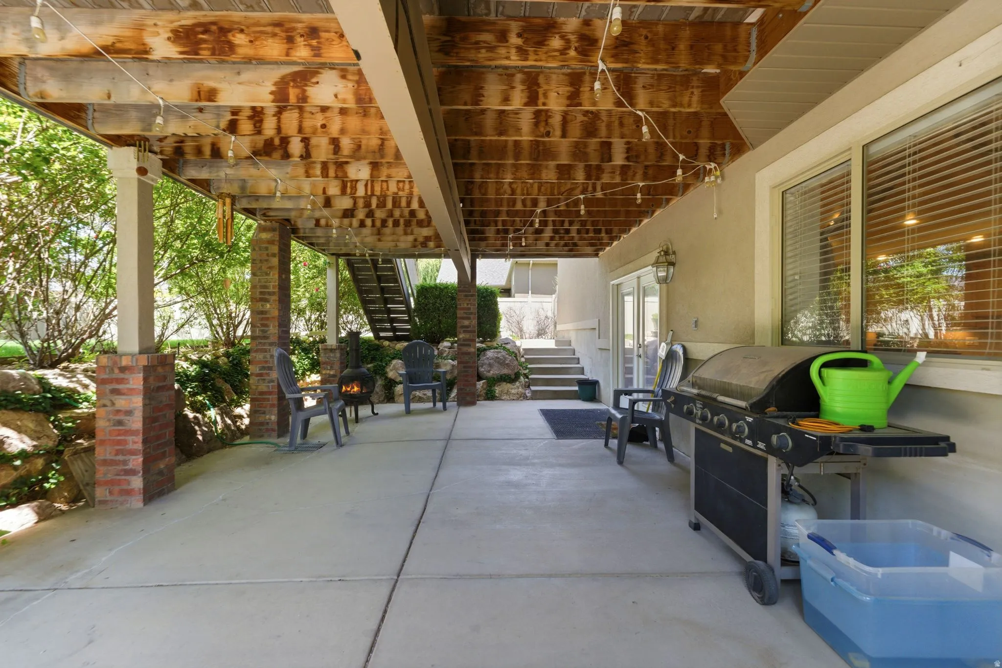 Expansive concrete patio with overhead deck structure, supported by brick-clad columns and white posts