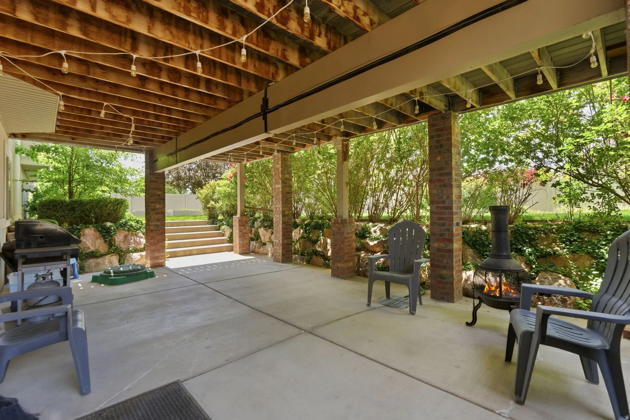 Concrete patio featuring a wood-beam ceiling, brick support columns, and string lighting