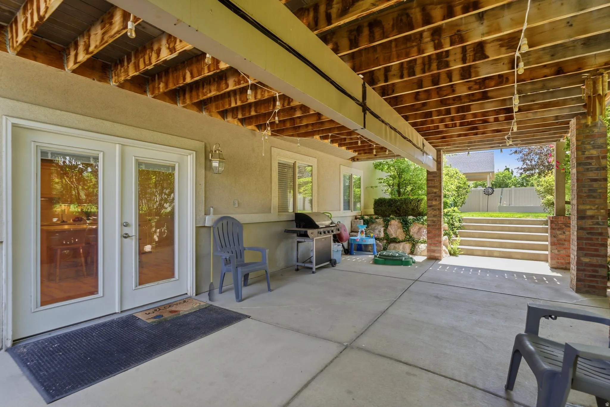 Covered concrete patio featuring exposed wood ceiling joists and brick columns