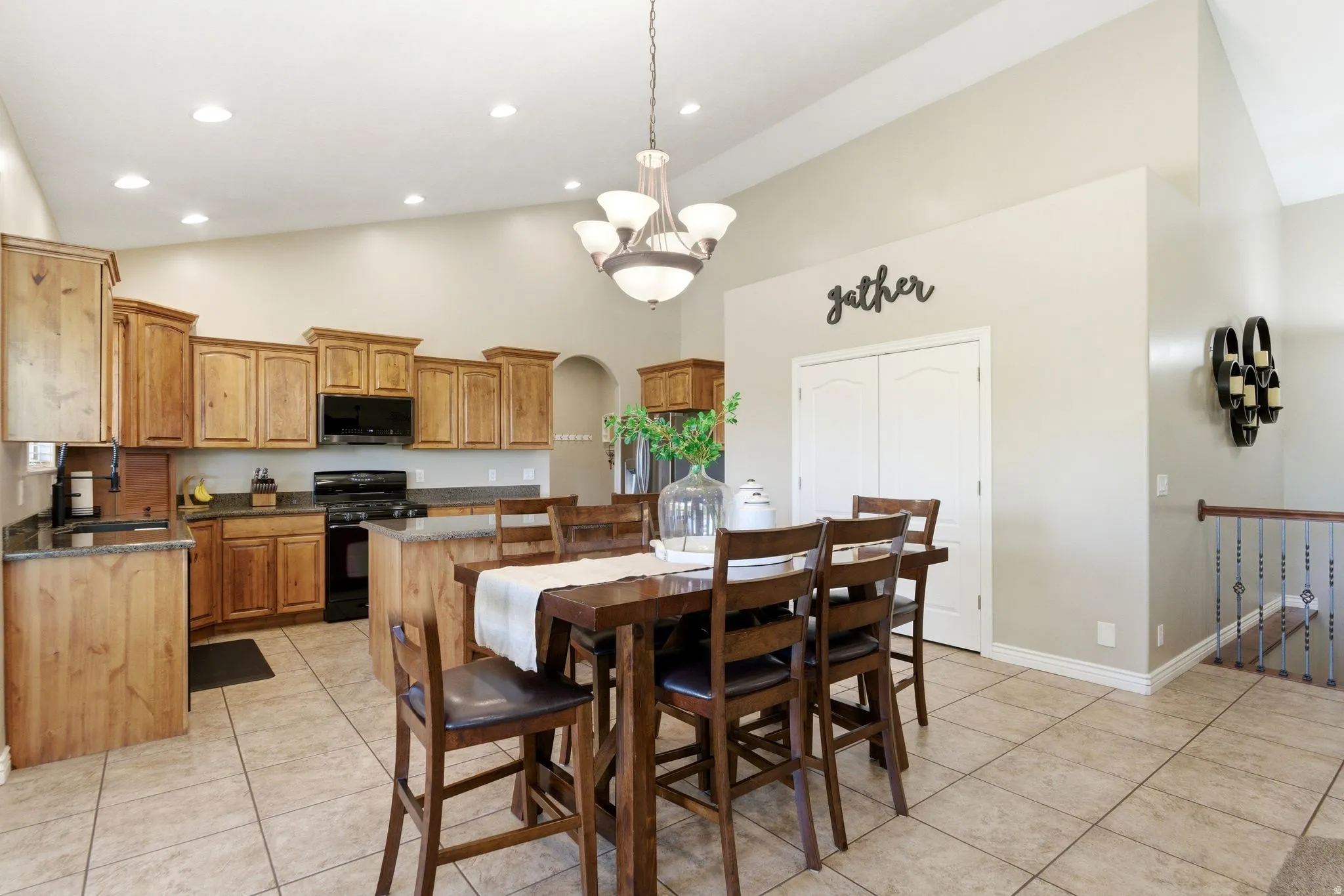 Open-concept kitchen and dining area featuring vaulted ceilings, recessed lighting, wood cabinetry, dark countertops, and tile flooring