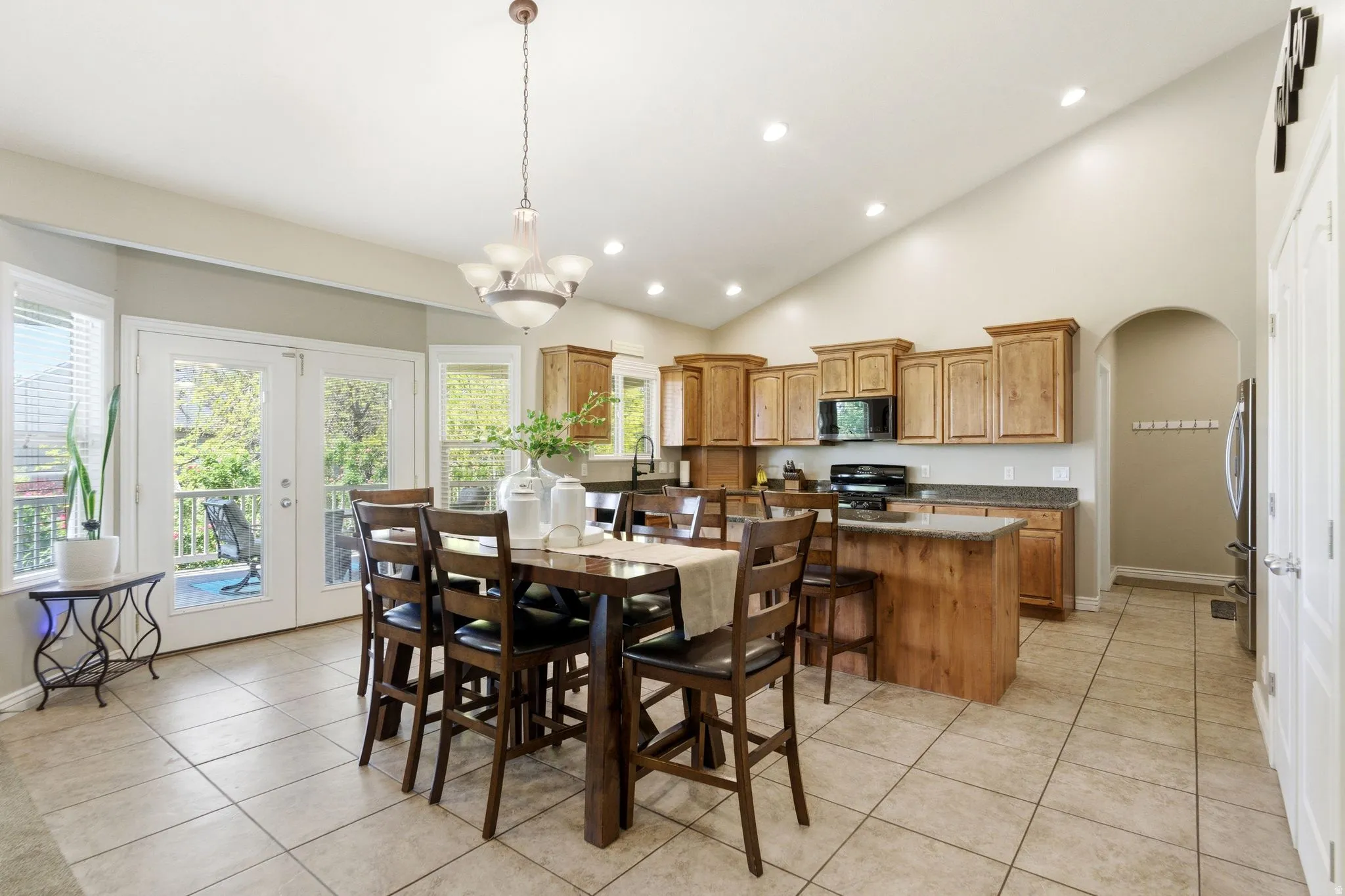Open-concept kitchen and dining area featuring vaulted ceilings, recessed lighting, double glass patio doors, wood cabinetry, and a kitchen island with stone countertops