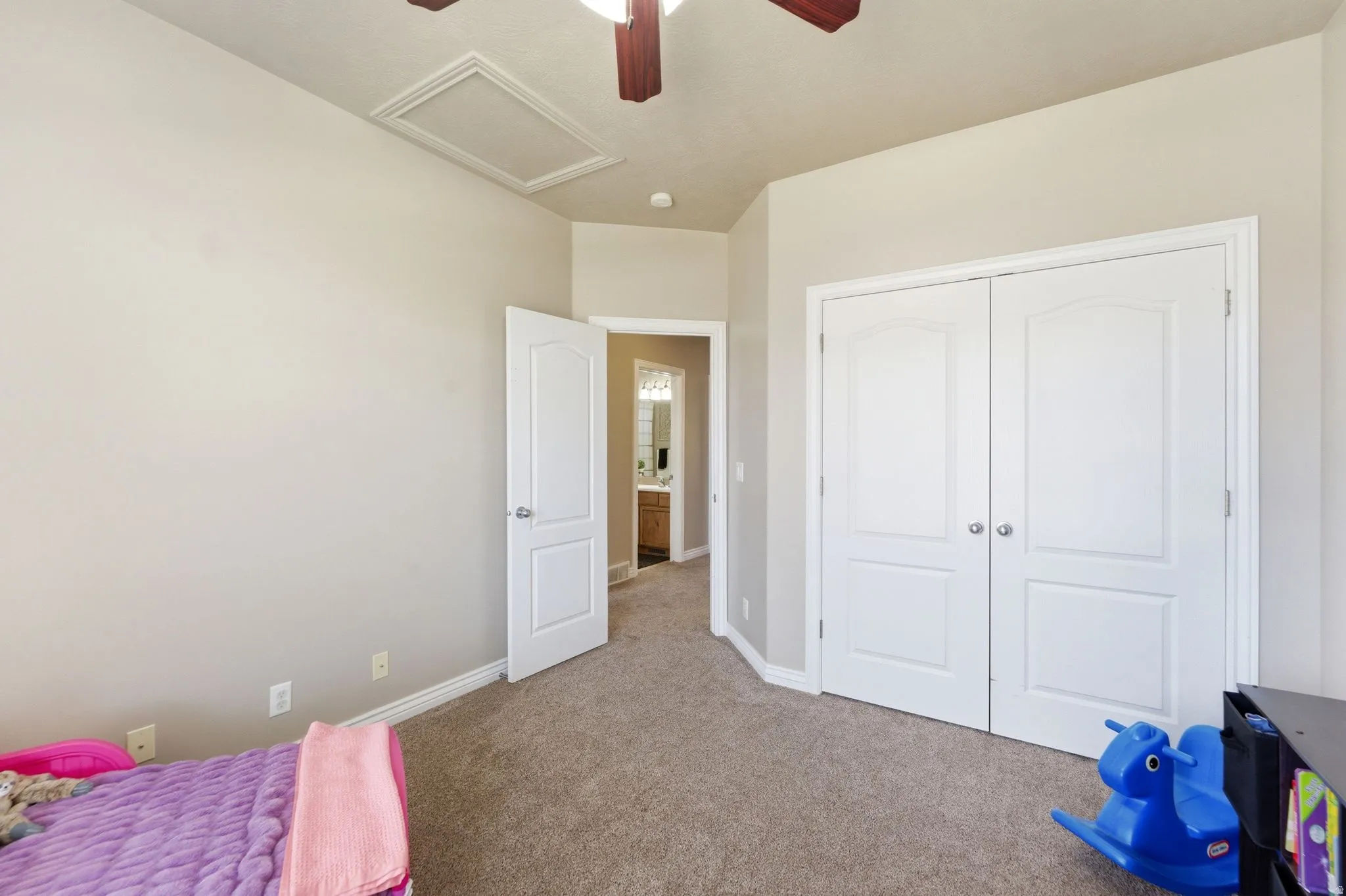 Carpeted room featuring a ceiling fan with wood-finish blades, white bi-fold closet doors, and light-toned walls
