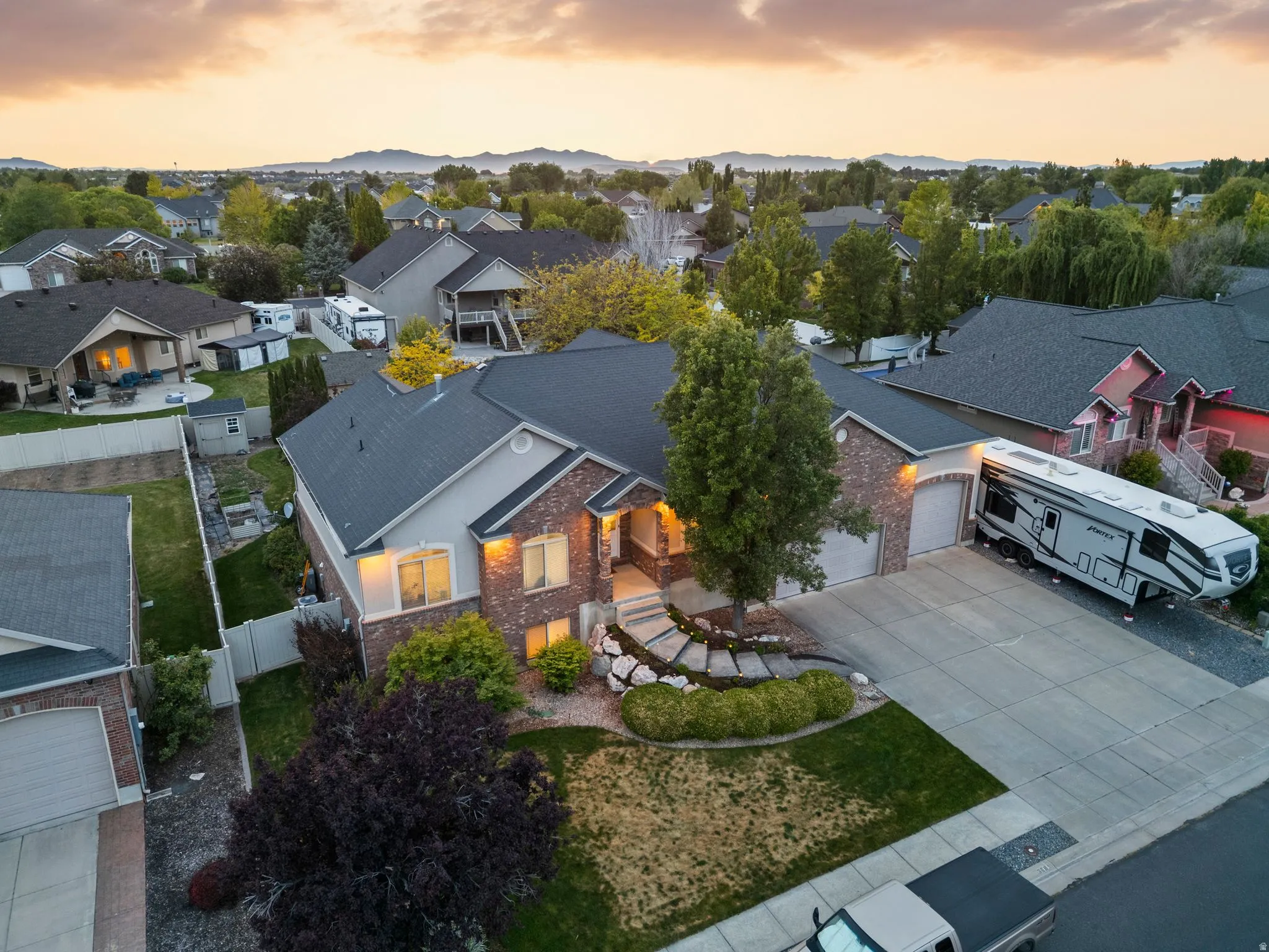 Front exterior featuring a brick and stucco facade, a two-car garage, mature landscaping, and an extended paved driveway