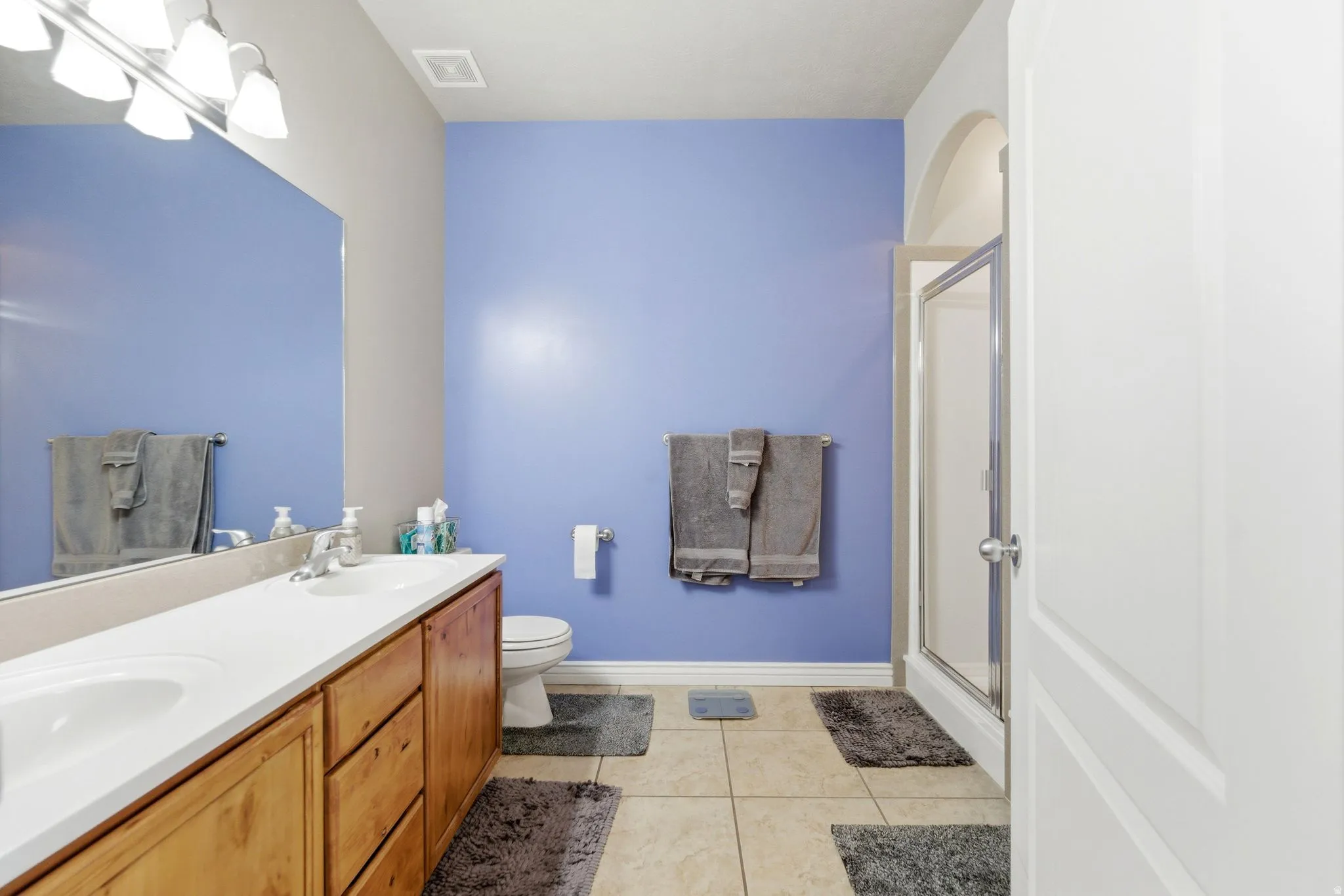 Bathroom featuring a double vanity with wood cabinetry, integrated white sinks, and a large mirror