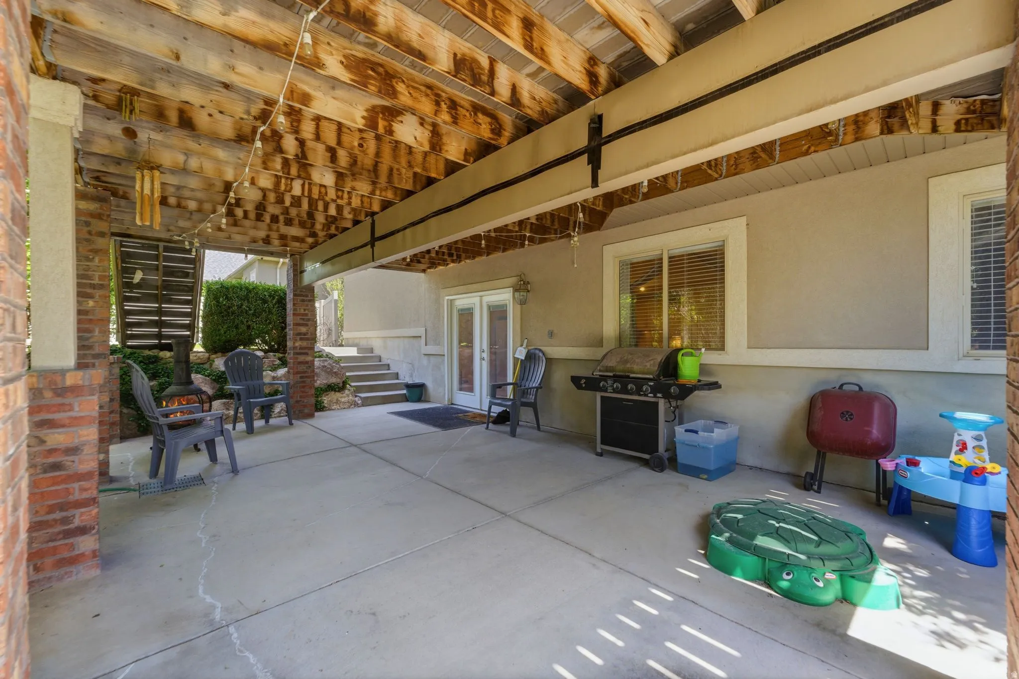 Covered patio featuring a concrete surface, exposed wood ceiling, and brick support columns