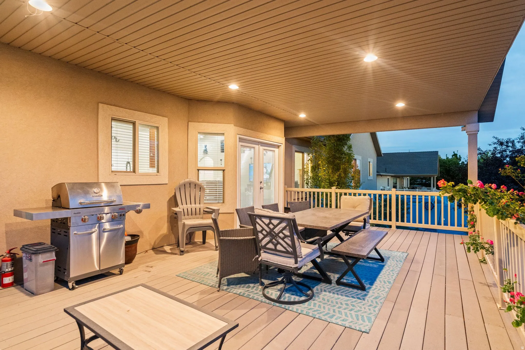 Spacious covered deck featuring composite decking, recessed lighting, white railing, and exterior wall-mounted lights